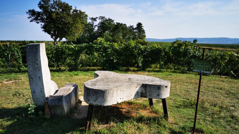 Steinbank und Tisch in einem Weinberg mit Schild 'Geheimtipp'.