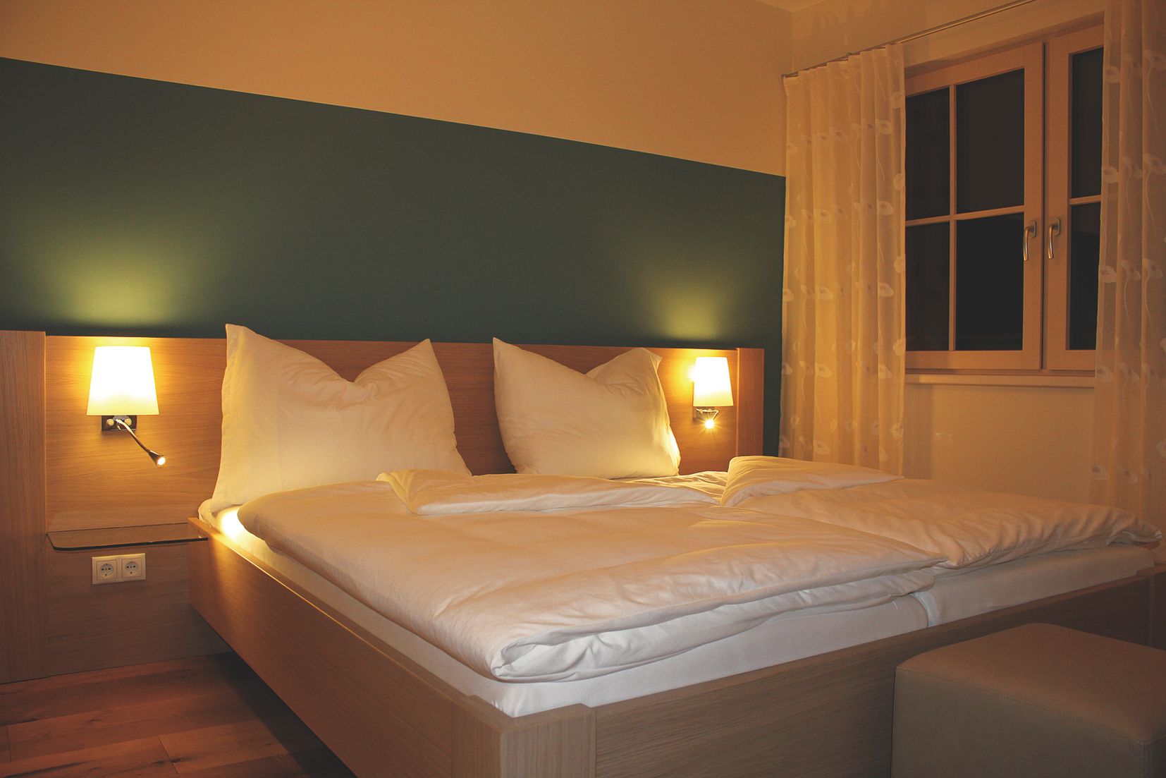 Ein gemütliches Gästezimmer mit einem Doppelbett, zwei Nachttischlampen und einem Fenster mit Vorhängen.