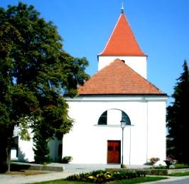 Wei&szlig;e Kirche mit rotem Dach und Turm, umgeben von B&auml;umen.