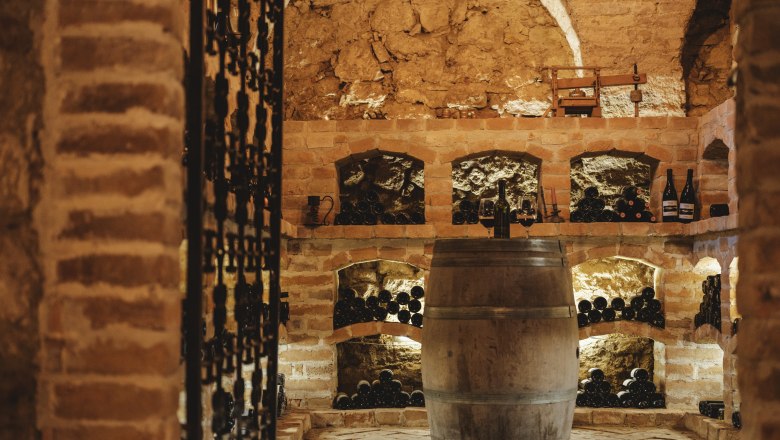Ein rustikaler Weinkeller mit Ziegelwänden, Weinregalen und einem Holzfass in der Mitte.
