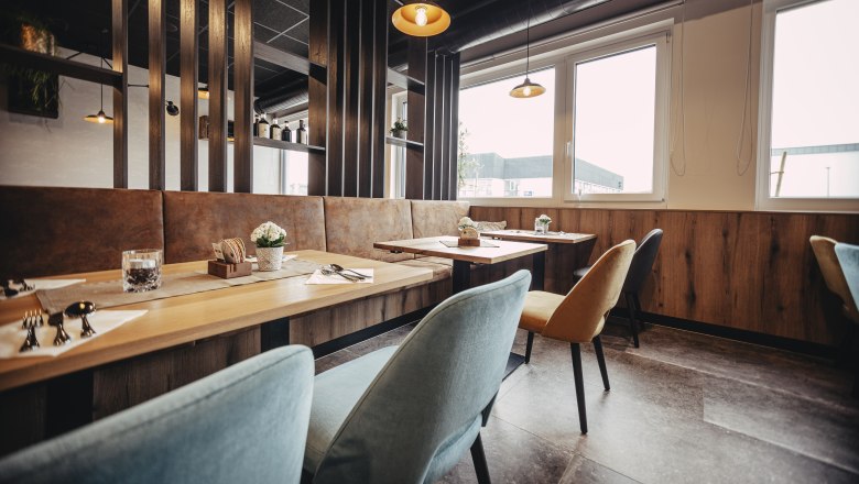 Modern eingerichtetes Restaurant mit Holztischen, bunten Stühlen und großen Fenstern.