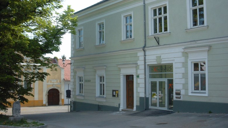 Ein zweistöckiges, hellgrünes Gebäude mit der Aufschrift 'Haus' über der Tür.