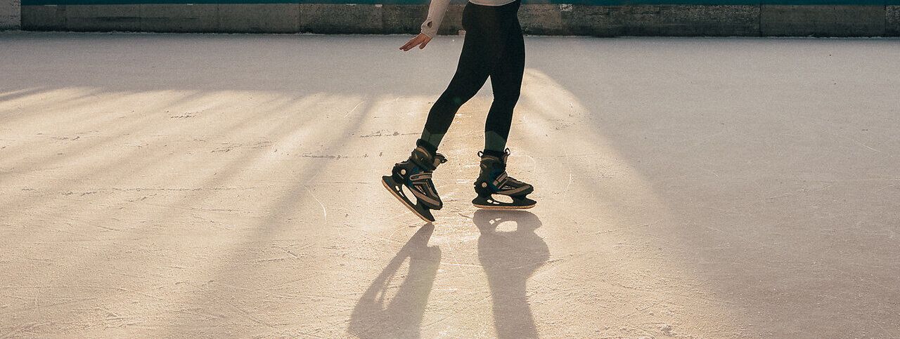 Ein strahlender Wintertag lädt zum Eislaufen ein, während die Sonne hinter den Bäumen aufgeht und eine magische Atmosphäre schafft. Die glitzernde Eisfläche spiegelt die warmen Farben des Himmels wider und verspricht unvergessliche Momente auf den Schlittschuhen.