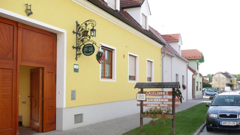 Gelbes Geb&auml;ude mit Schild 'G&auml;stezimmer Buschenschank Weinbau Poys' und geparktem Auto davor.