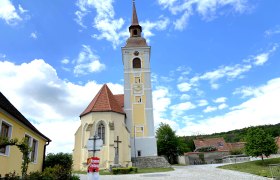 Kirche mit schiefem Turm in Waitzendorf, umgeben von blauen Himmel und Wolken.