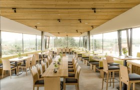 Innenansicht eines modernen Restaurants mit Holzmöbeln und großen Fenstern.