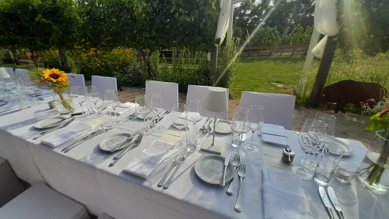 Elegante, gedeckte Tafel im Freien mit weißen Tischdecken und Sonnenblumen in einem Garten.