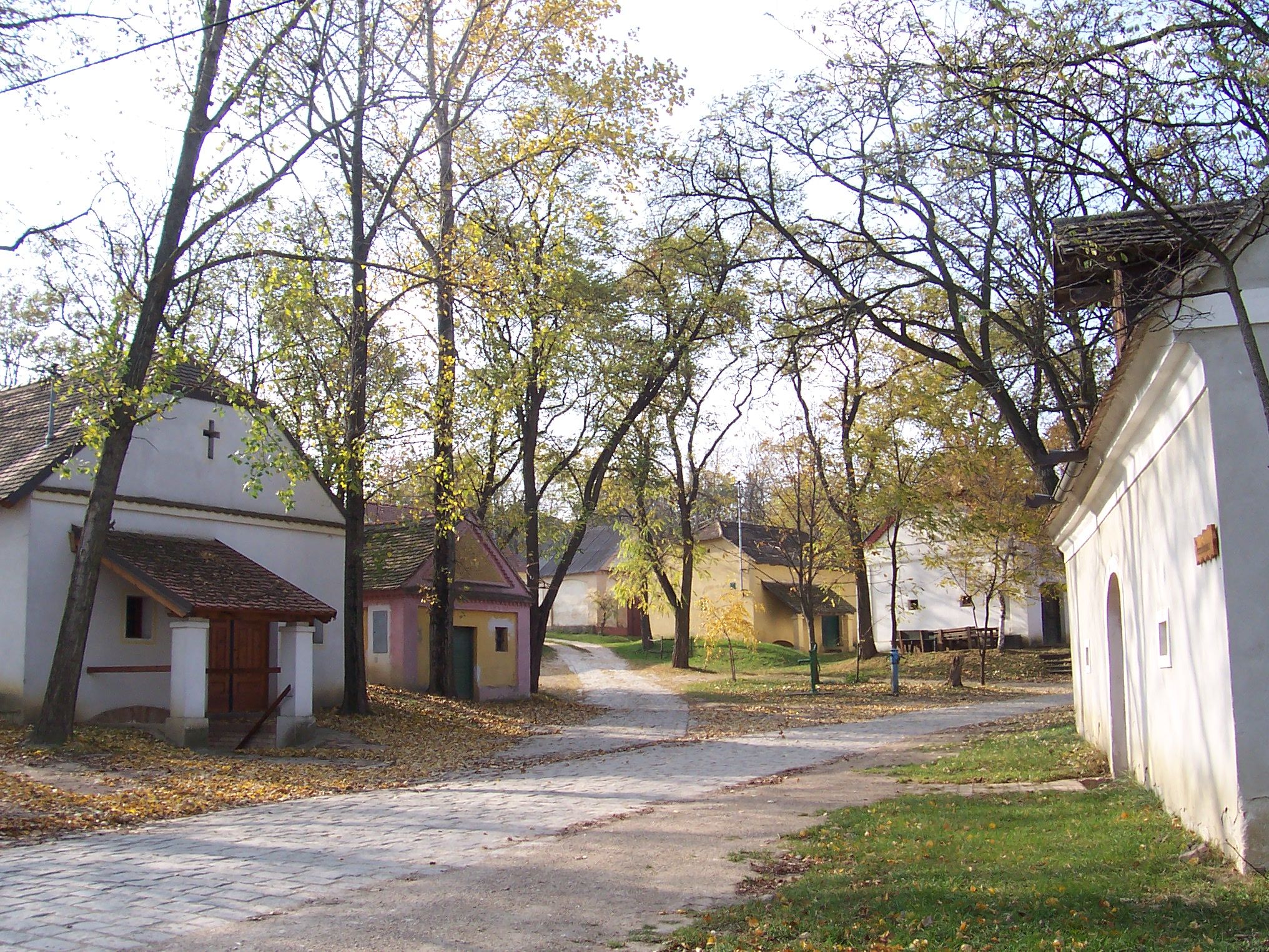 Ein ruhiger Dorfplatz mit kleinen, traditionellen Gebäuden und Bäumen im Herbst.
