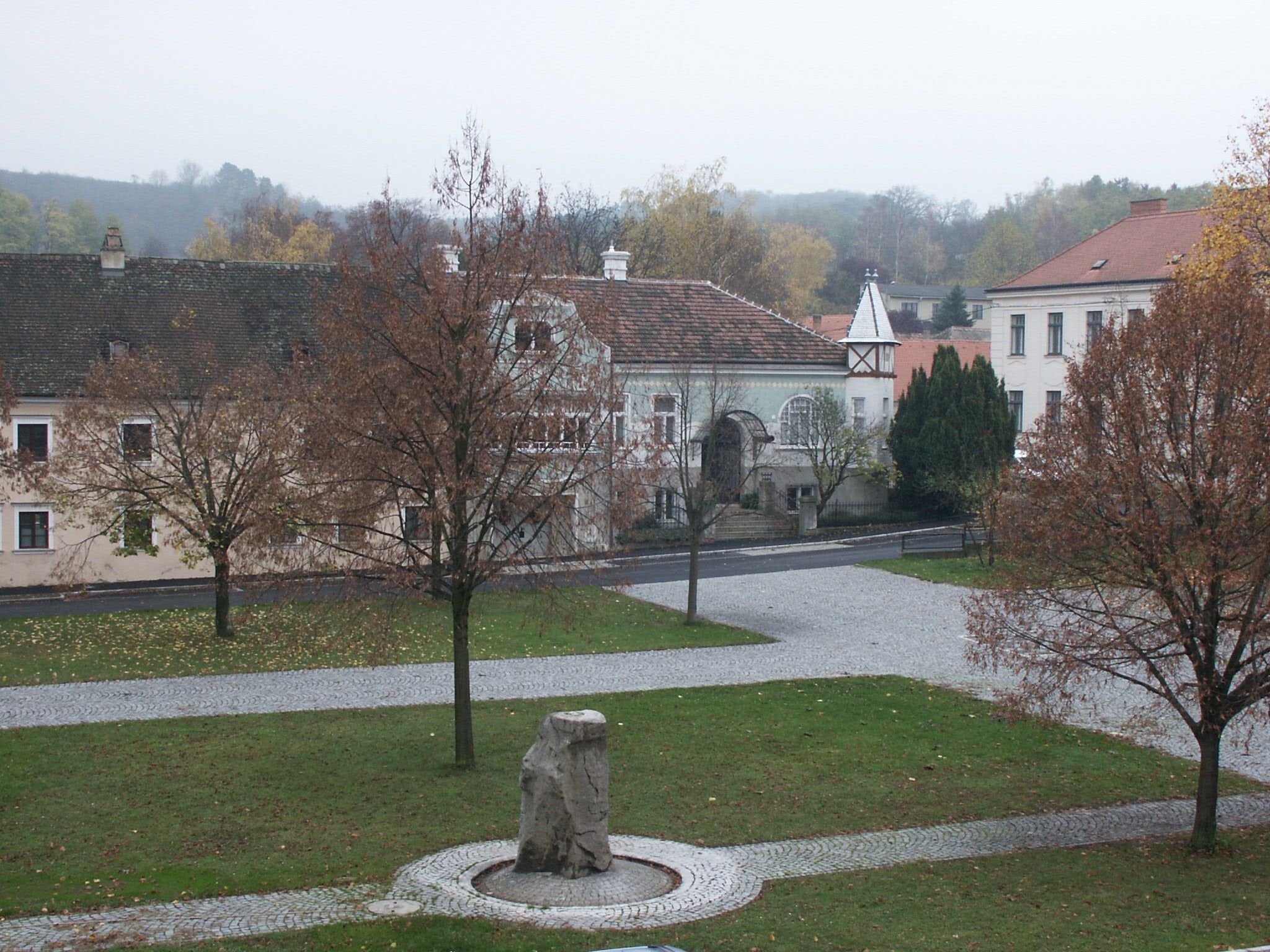 Hlavní náměstí Sitzendorf an der Schmida se stromy a kamenným pomníkem v popředí.