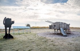 Spielplatz mit Holzspielgerät in Form eines Tieres und Katzenskulptur.