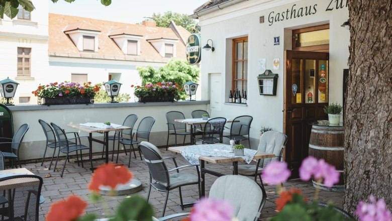 Schattiger Gastgarten mit Tischen und Stühlen vor einem Gasthaus.