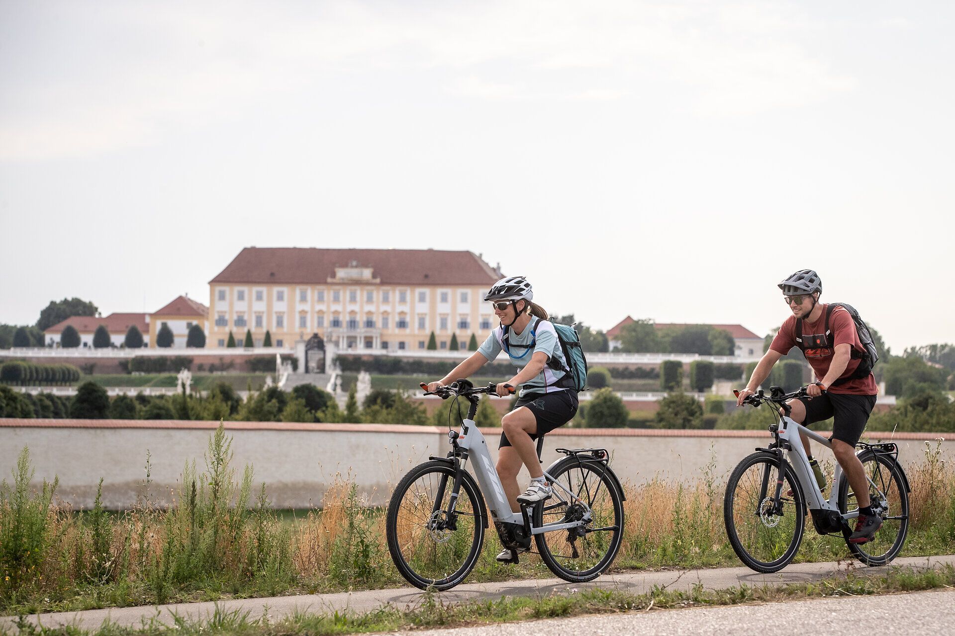 Zwei Radfahrer genießen die frische Luft und die malerische Landschaft entlang eines ruhigen Kanals. Die sanften Hügel im Hintergrund und die üppige Vegetation schaffen eine einladende Atmosphäre für Outdoor-Enthusiasten. Hier wird der Sommer in seiner schönsten Form erlebbar.