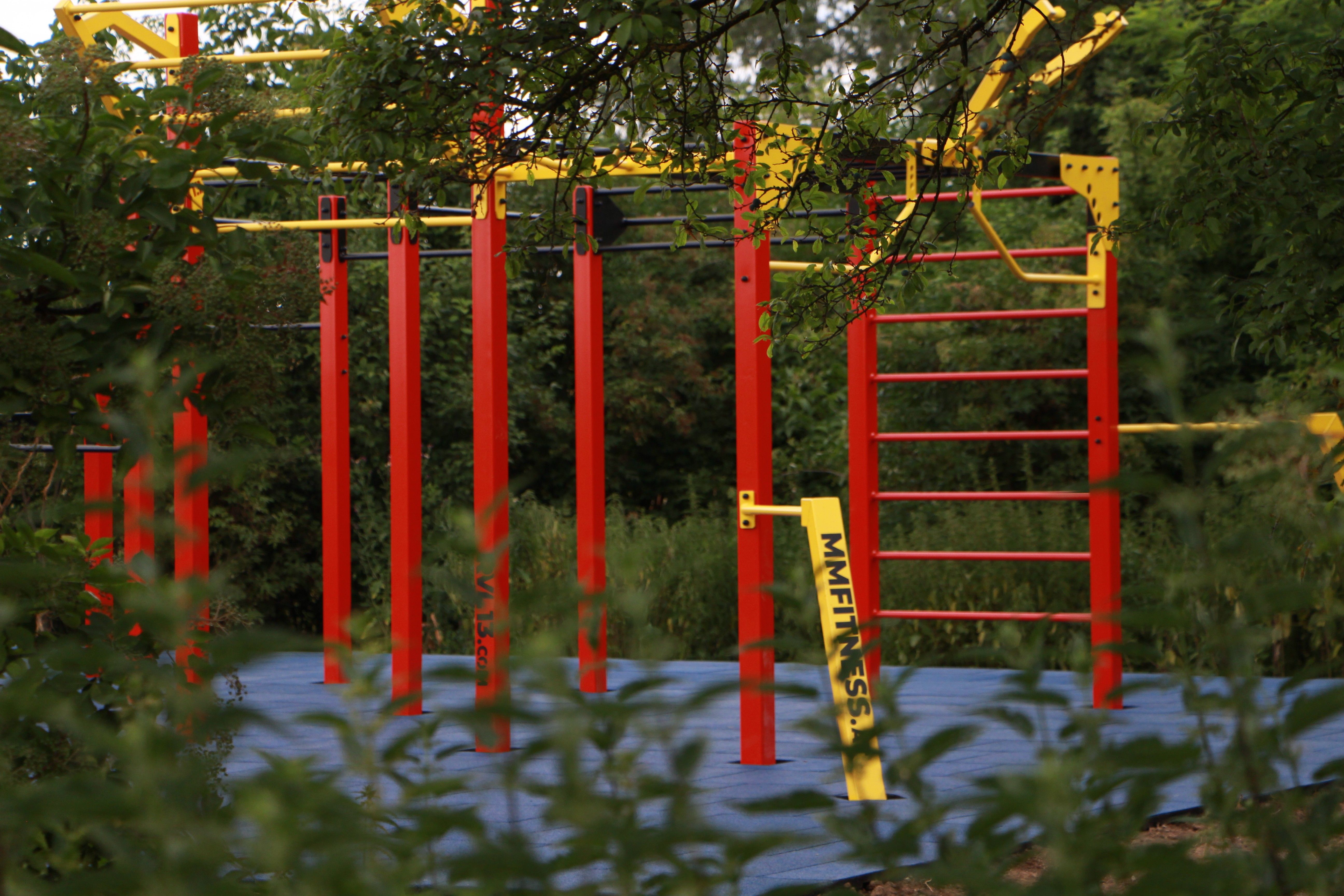 Ein Calisthenics-Park mit roten und gelben Stangen, umgeben von grüner Vegetation.