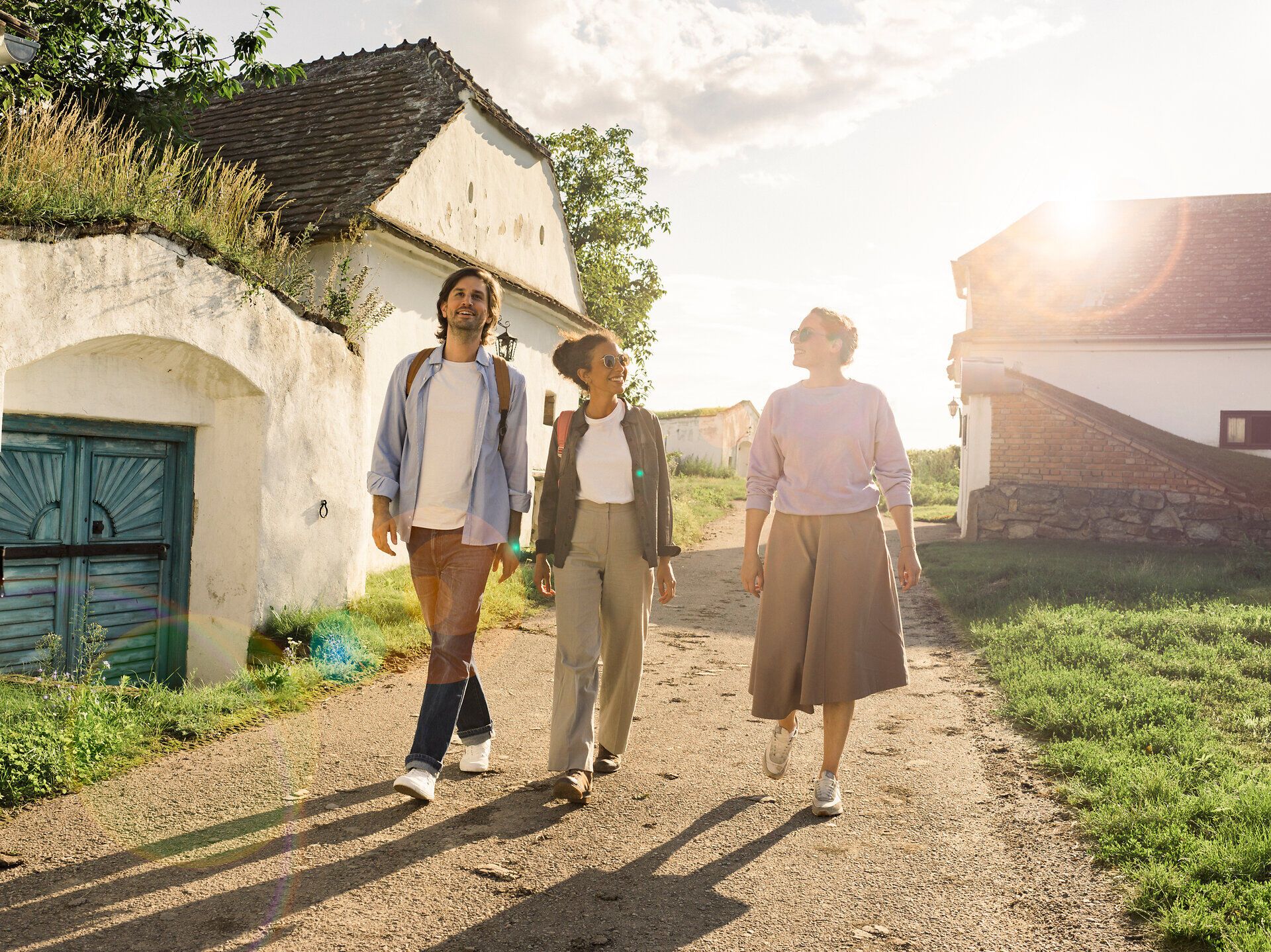 In der malerischen Kellergasse Maulavern schlendern drei Freunde entspannt den Weg entlang, umgeben von den sanften Hügeln des Weinviertels. Die warmen Sonnenstrahlen tauchen die Szenerie in ein goldenes Licht und laden dazu ein, die köstlichen Weine der Region zu entdecken.