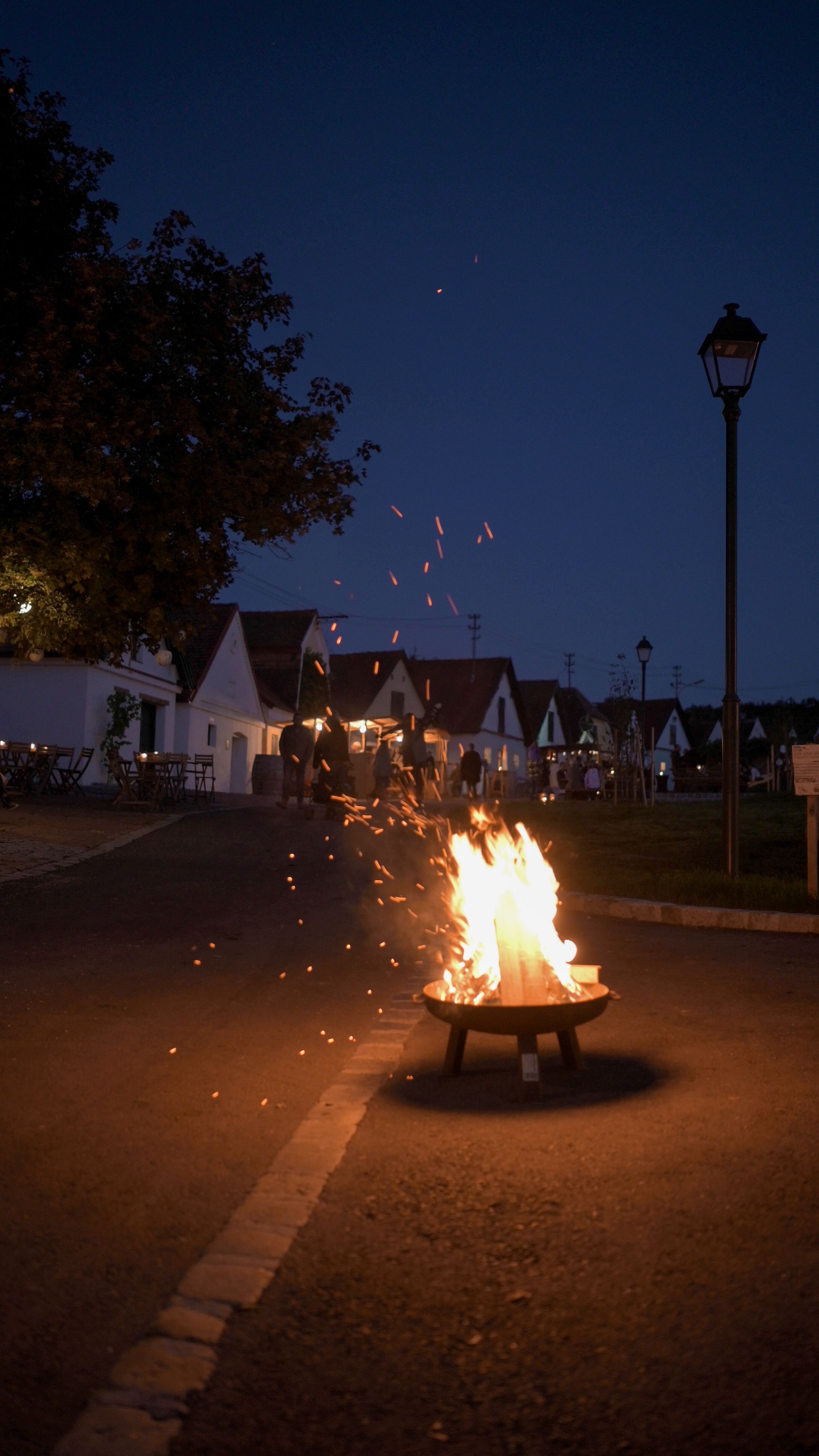 Eine romantische Nacht entfaltet sich unter dem klaren Sternenhimmel, während das sanfte Licht der Flammen die Umgebung in warmen Tönen erleuchtet. Die Atmosphäre ist erfüllt von der Vorfreude auf Wein und Kunst, die hier in der Kellergasse zelebriert werden.