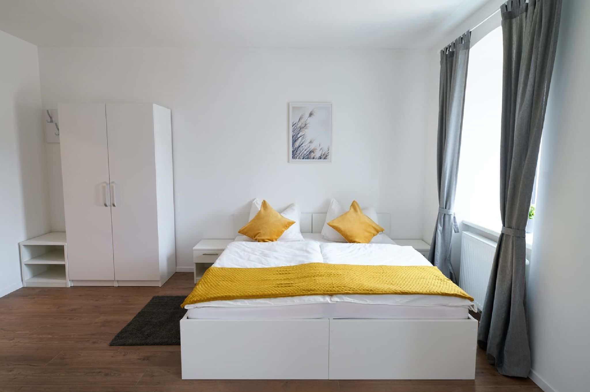 Modernes Doppelzimmer mit weißem Bett, gelben Kissen und grauen Vorhängen.