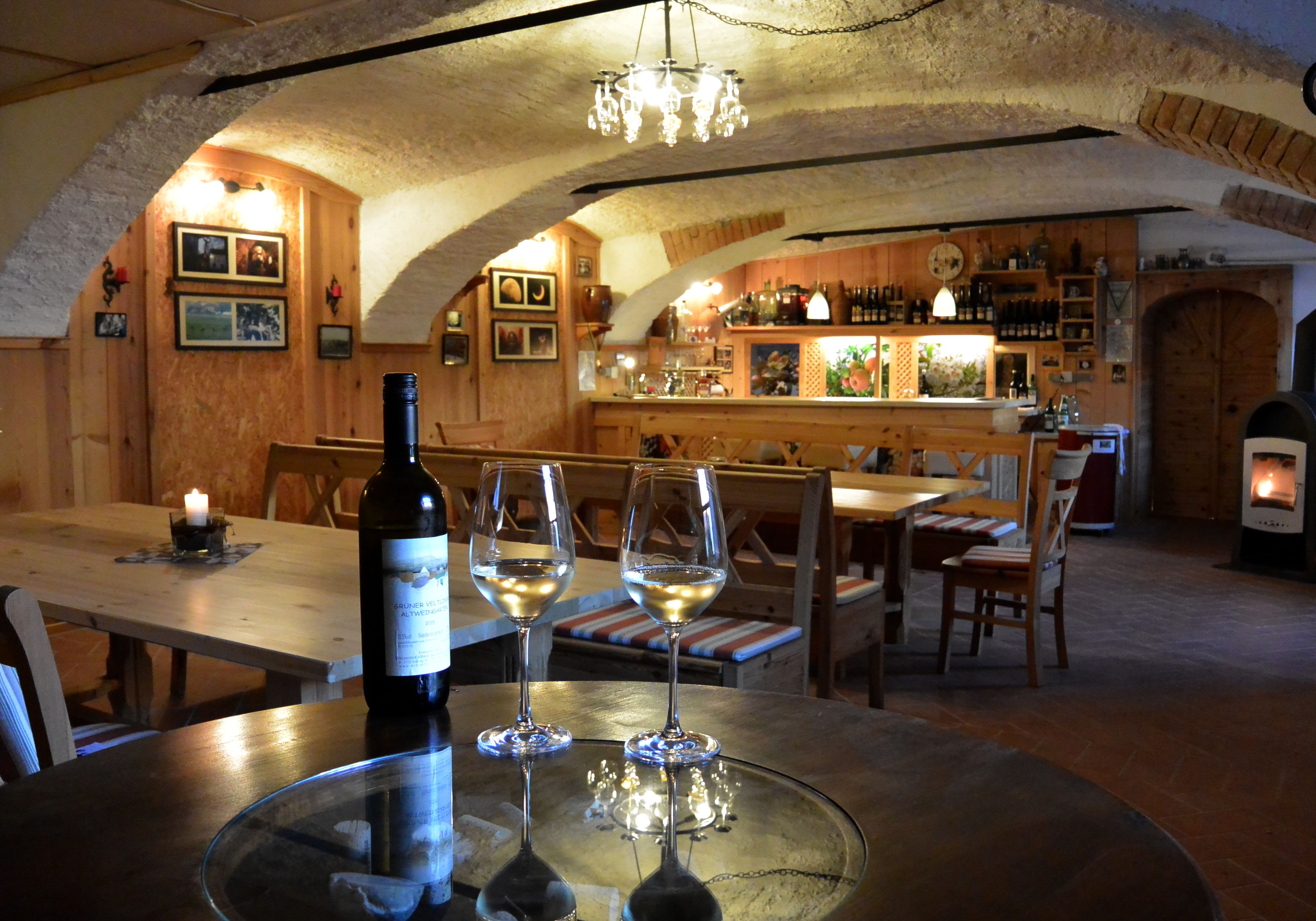 Útulná vínna pivnica s dreveným nábytkom, fľašami a pohármi na stole.