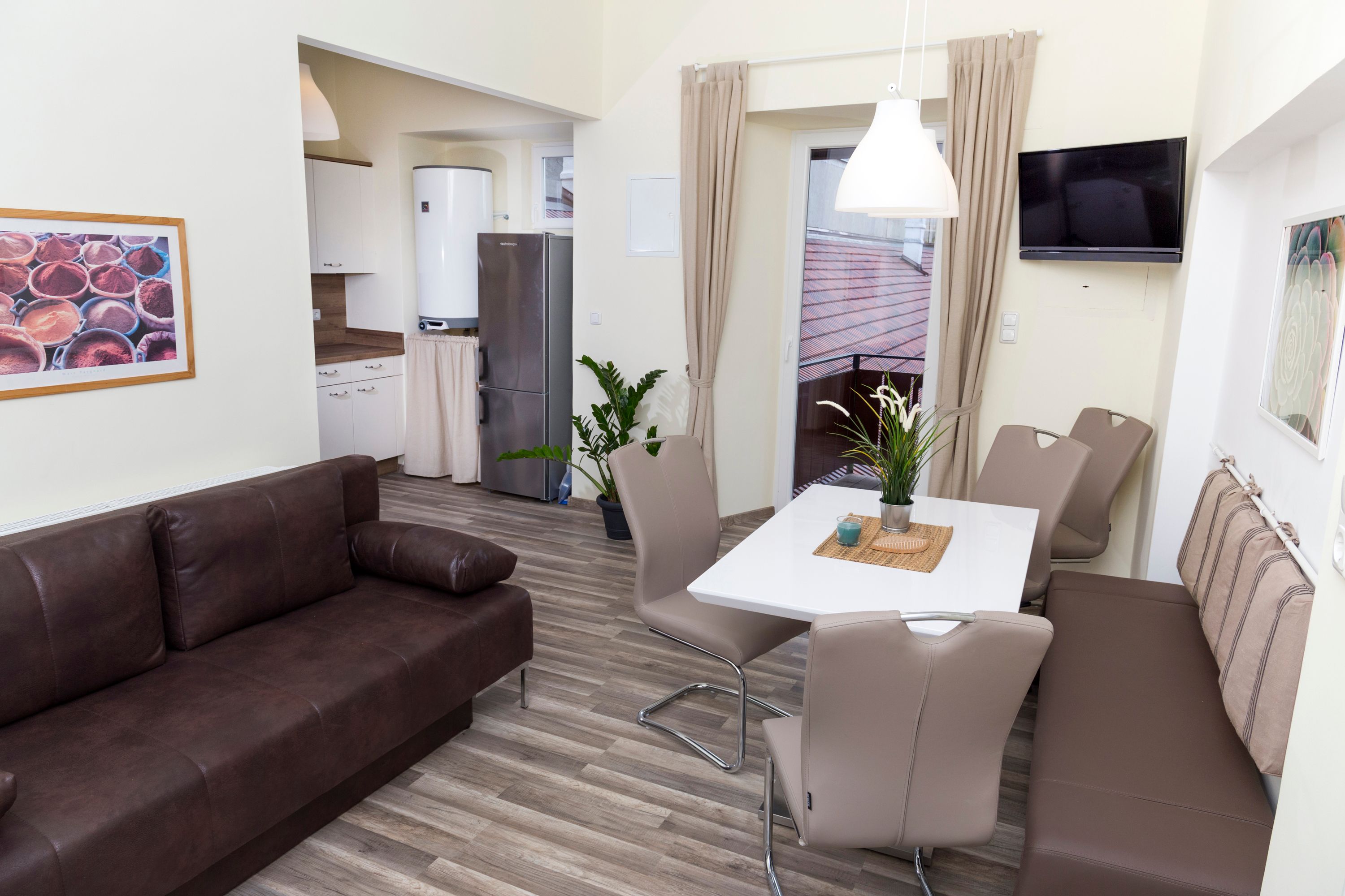 Moderne Küche mit braunem Sofa, Esstisch und Stühlen, Kühlschrank und Pflanzen.