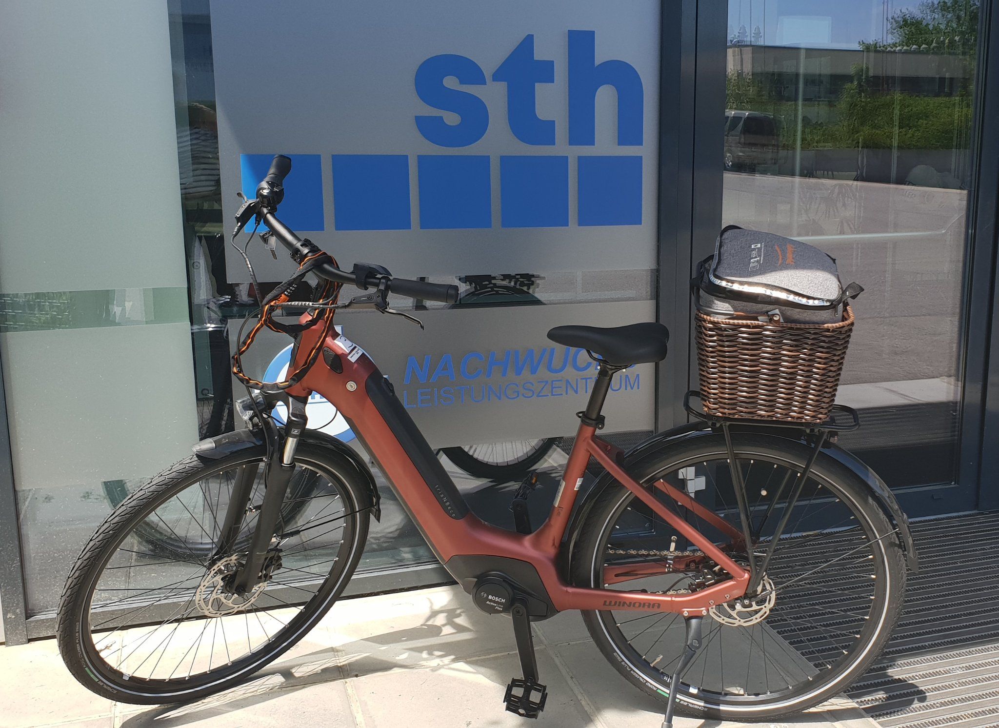 Ein rotes E-Bike steht vor einem Gebäude mit der Aufschrift 'sth Nachwuchsleistungszentrum'.