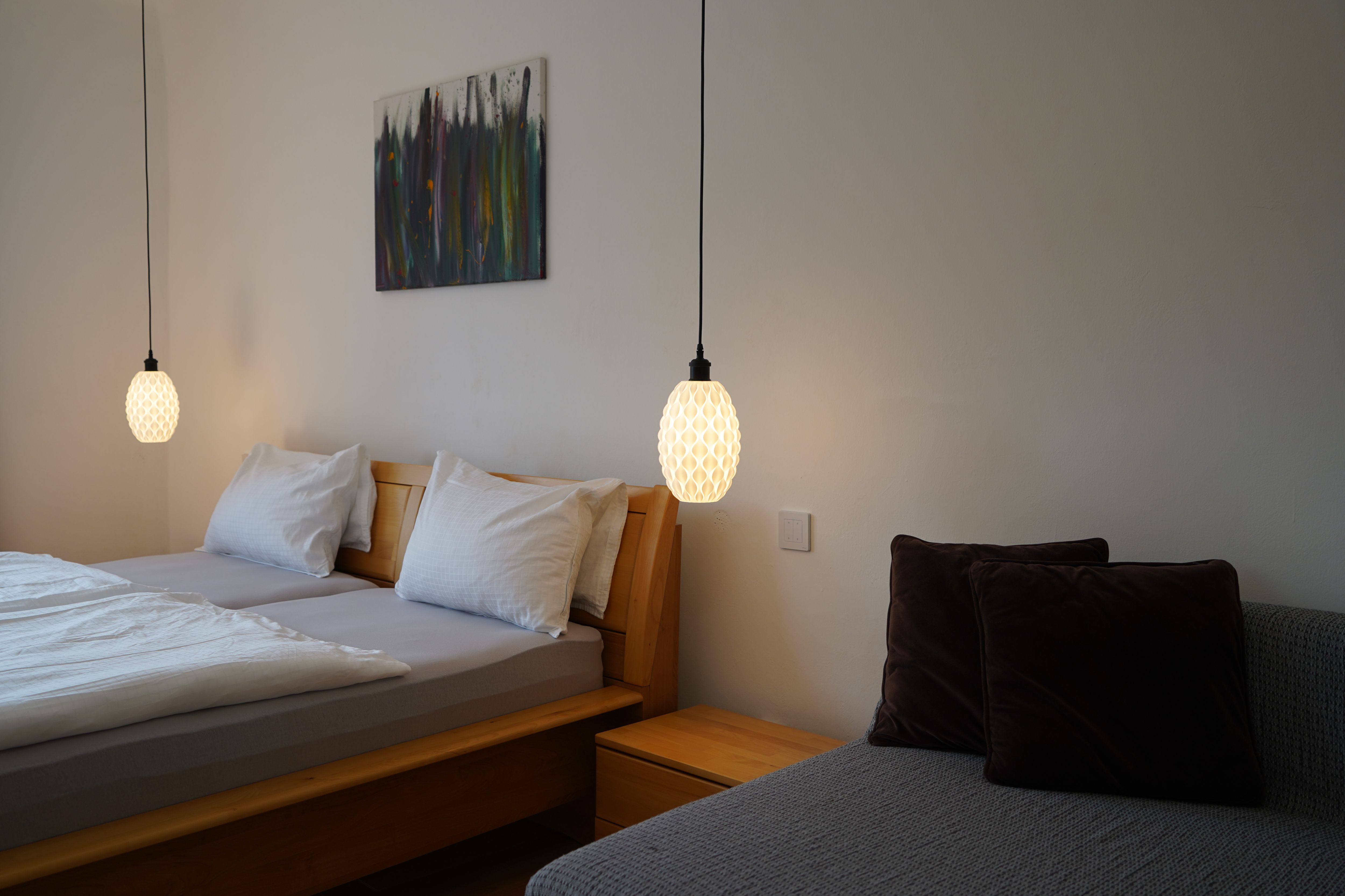 Schlafzimmer mit Doppelbett, zwei Hängelampen und einem Sofa mit Kissen.