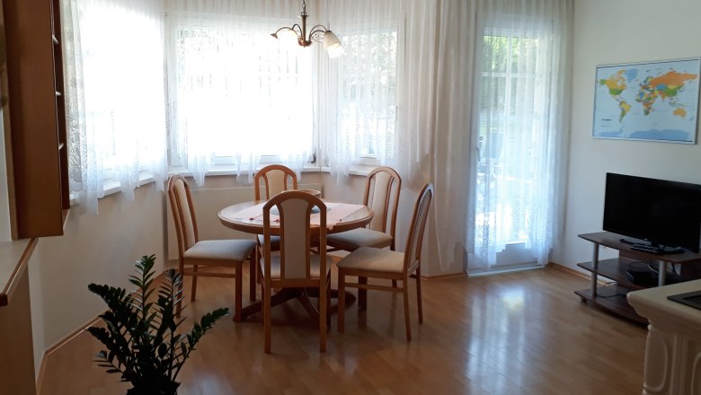 Helle Wohnküche mit Esstisch, Stühlen, TV und Weltkarte an der Wand.