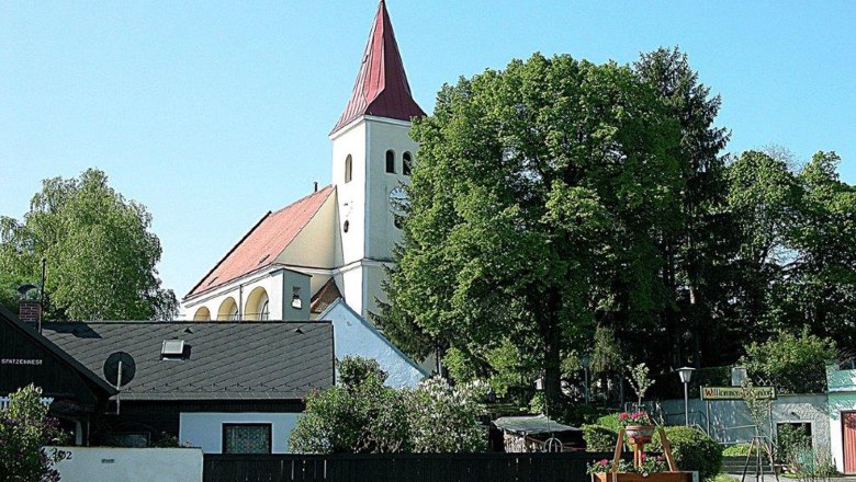 A church with a red roof and tower, surrounded by trees and houses.