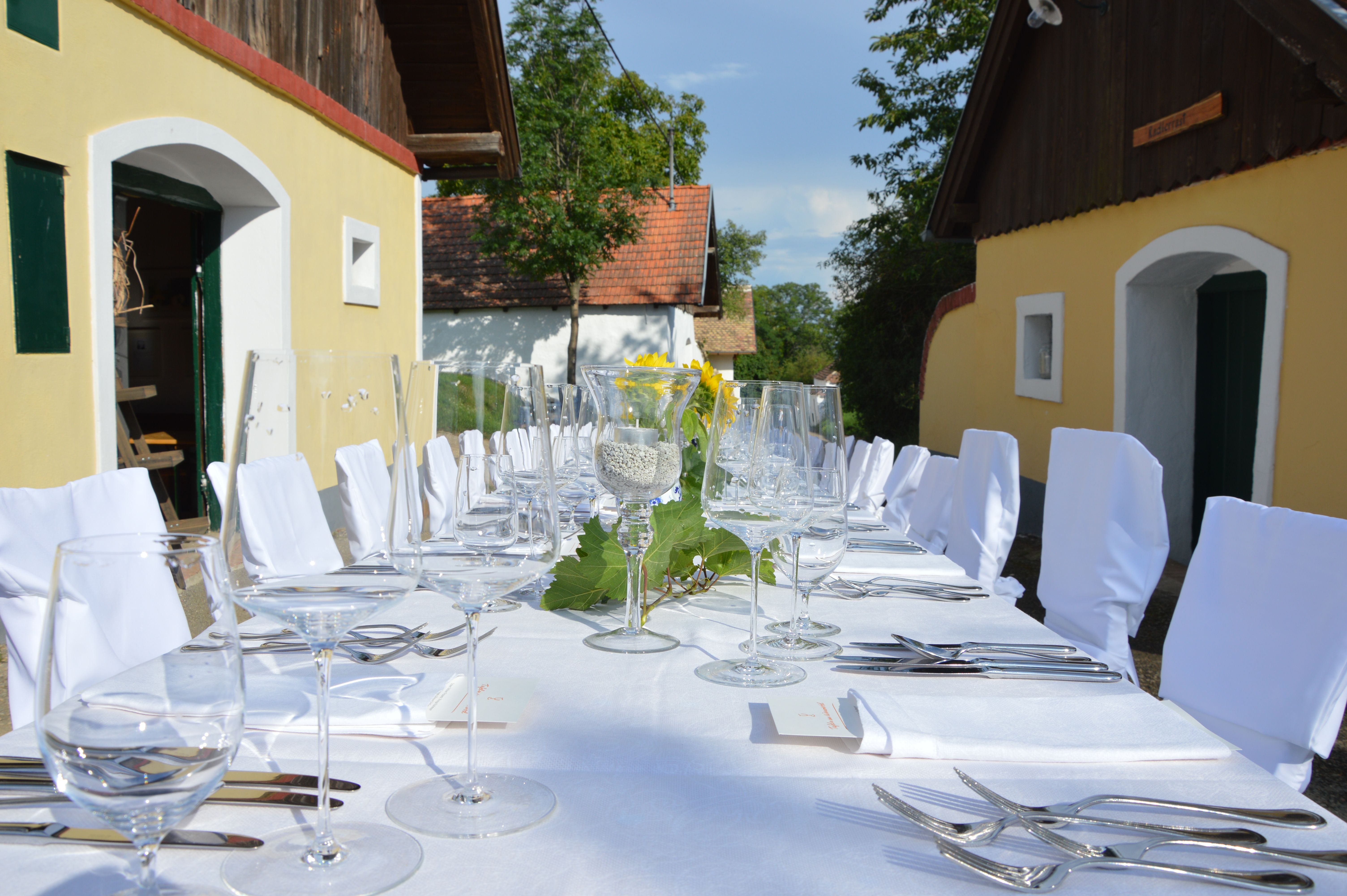 Ein festlich gedeckter Tisch im Freien mit weißen Tischdecken und Stühlen, umgeben von traditionellen Gebäuden.