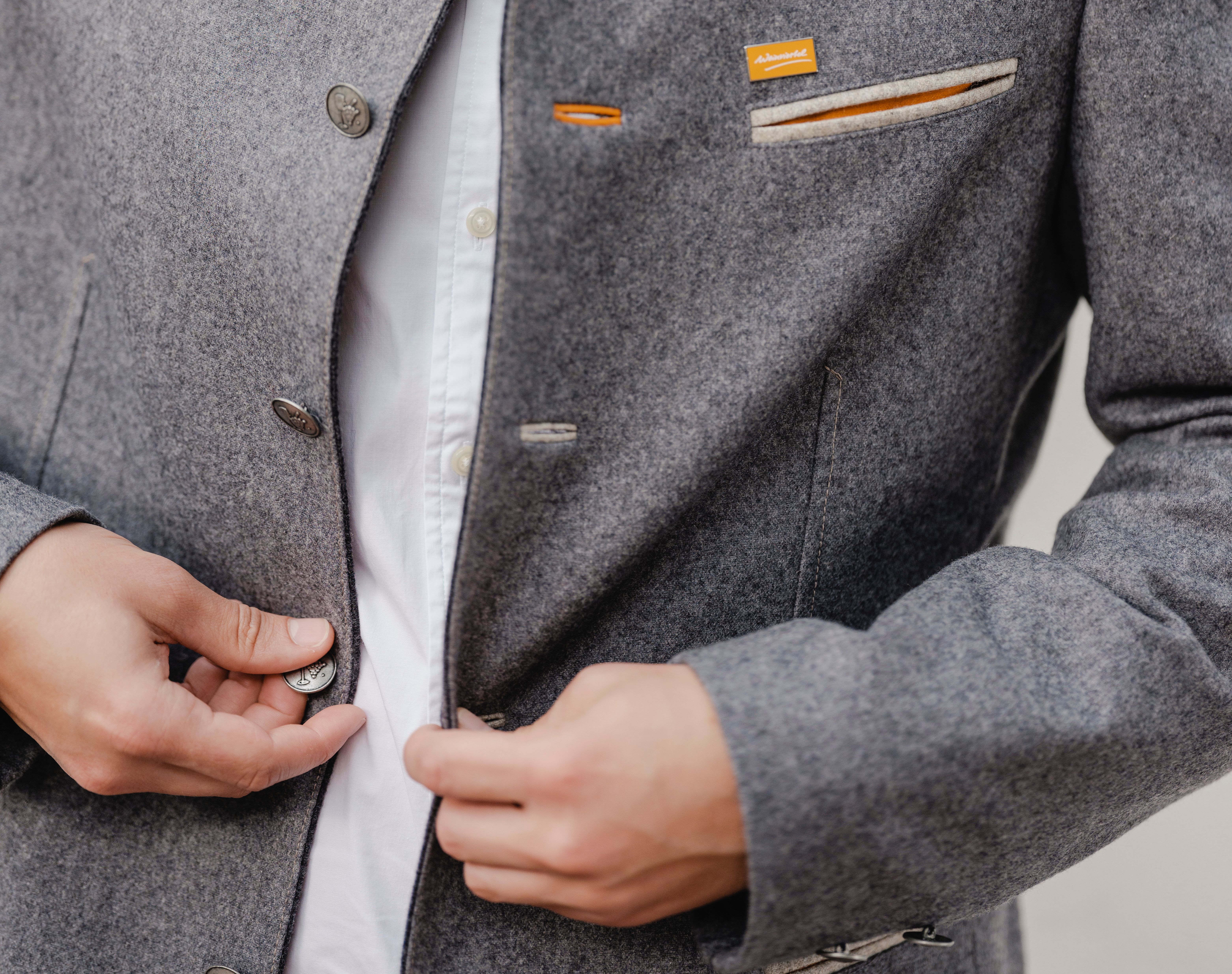 Ein Mann knöpft an seinem grauen Trachtenjanker einen Knopf zu.