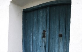 Blaue Holztür in einem weißen Gebäude mit Kopfsteinpflaster davor.