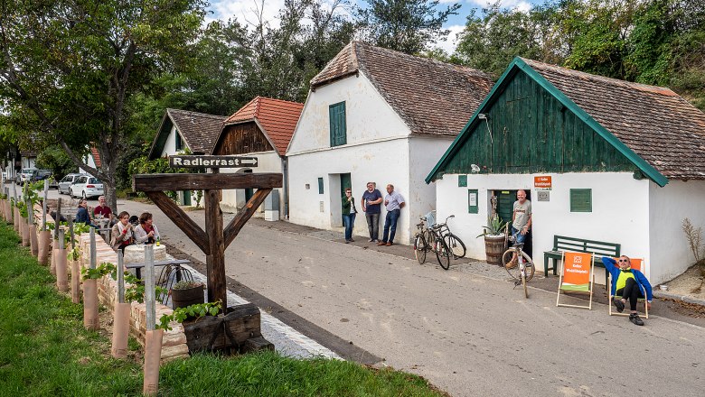 Weinkellerstraße in Mailberg mit Menschen, Fahrrädern und einem Schild 'Radlerrast'.