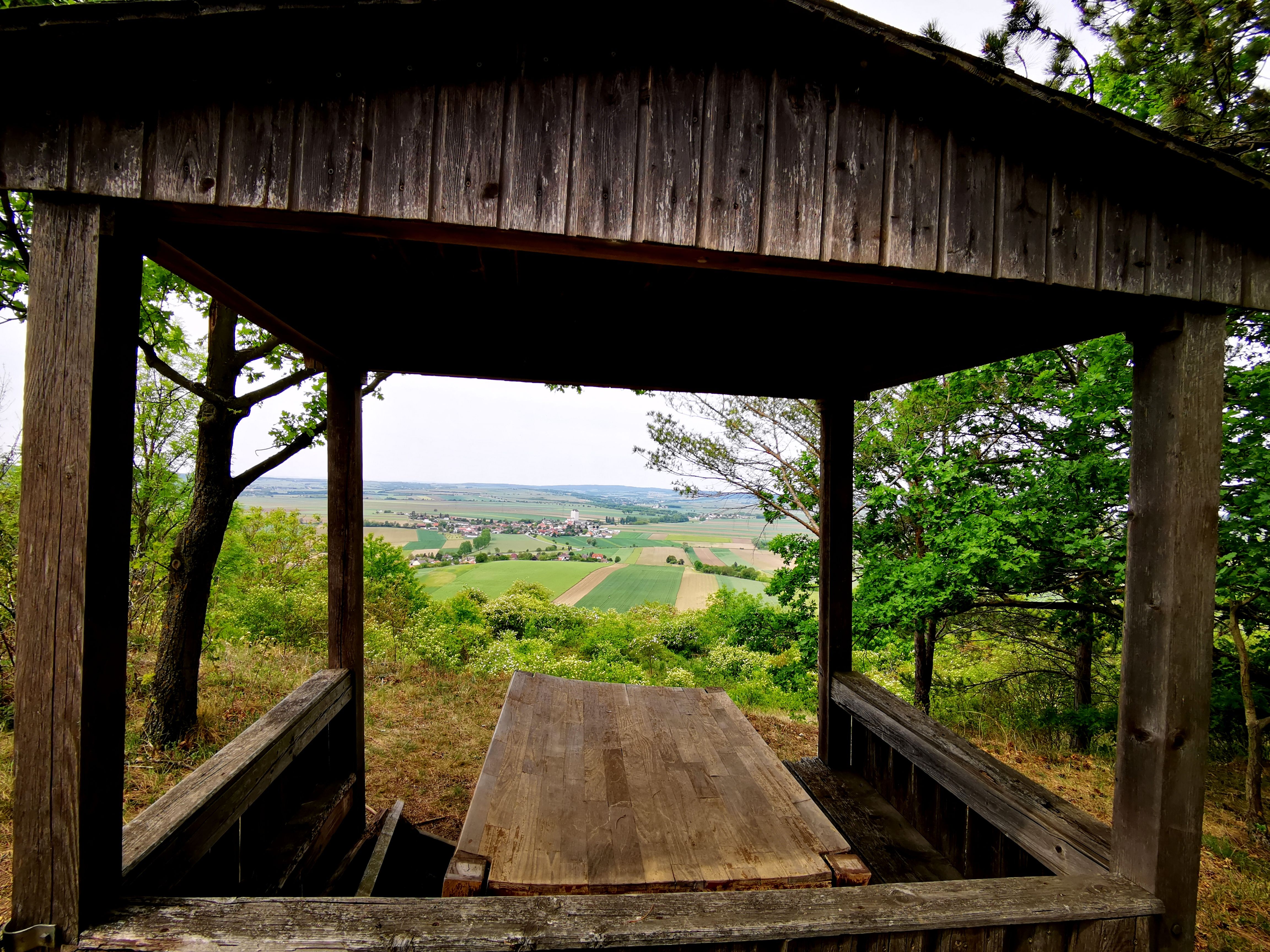 Holzhütte mit Blick auf Felder und Dorf in der Ferne.