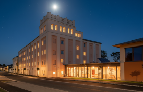 Ein beleuchtetes Geb&auml;ude bei Nacht mit einem hellen Mond am Himmel.