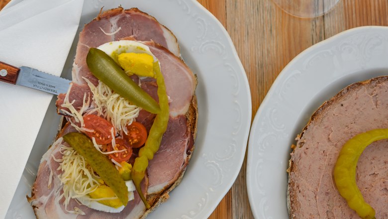 Two plates with sandwiches and two glasses of white wine on a wooden table.