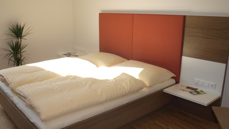 Modernes Gästezimmer mit Doppelbett, rotem Kopfteil und Pflanzen.