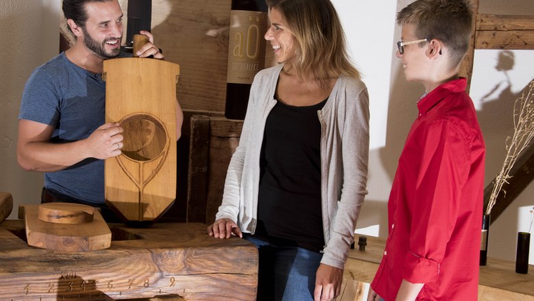 Three people are standing around a wooden table, one person is holding a wooden board with an engraving.