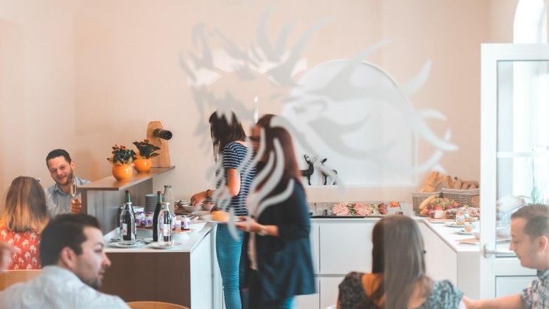 Menschen bedienen sich an einem Frühstücksbuffet in einem hellen Raum.