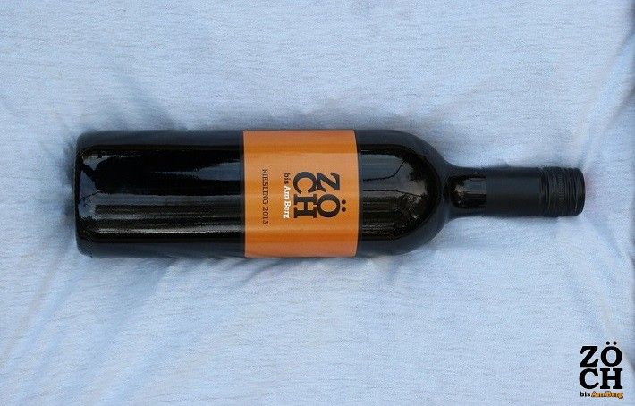 A wine bottle with an orange Zöch brand label on a light background.