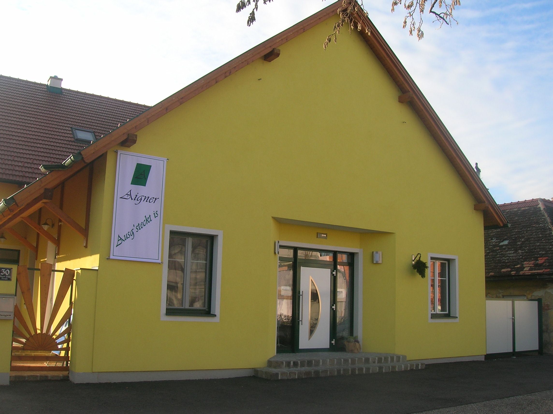 Gelbes Gebäude mit einem Schild "Aigner Ausg'steckt is" an der Fassade.