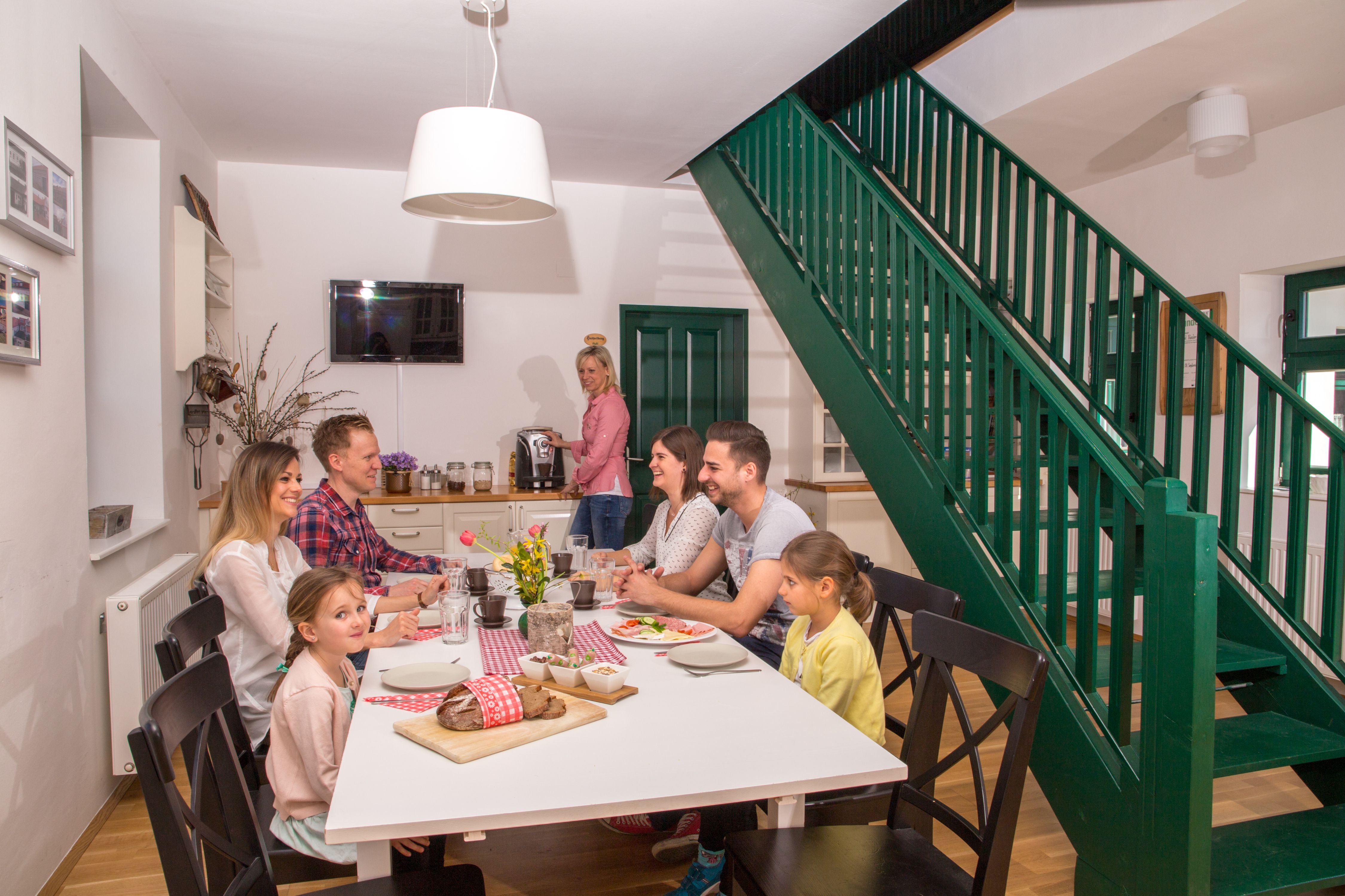 Familie sitzt an einem Tisch in einem modernen Esszimmer mit grüner Treppe.