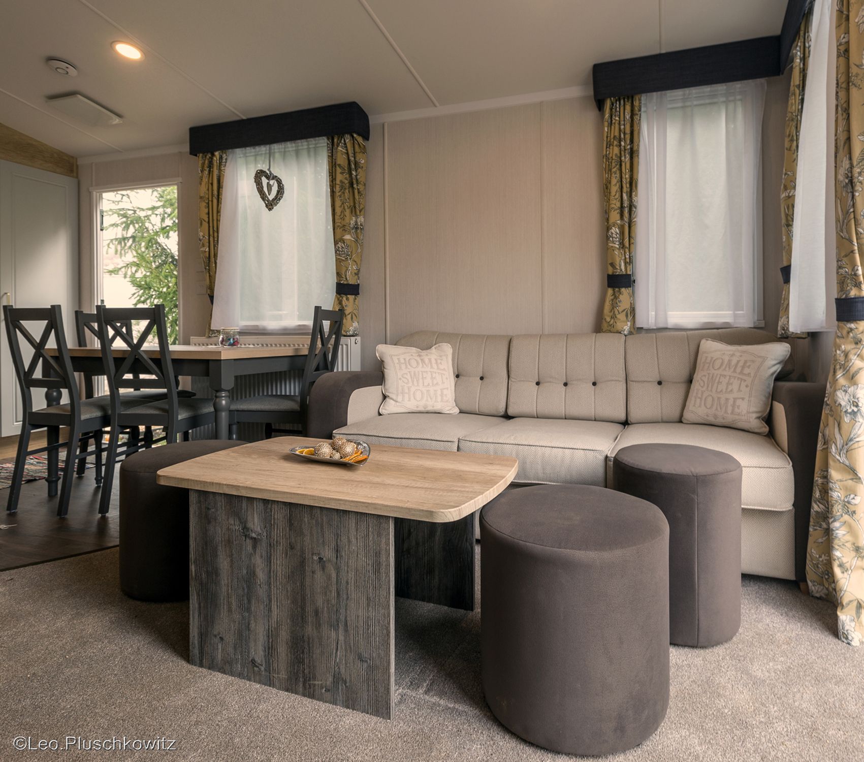 Gemütliches Wohnzimmer mit beiger Couch, Holztisch und Essbereich im Hintergrund.