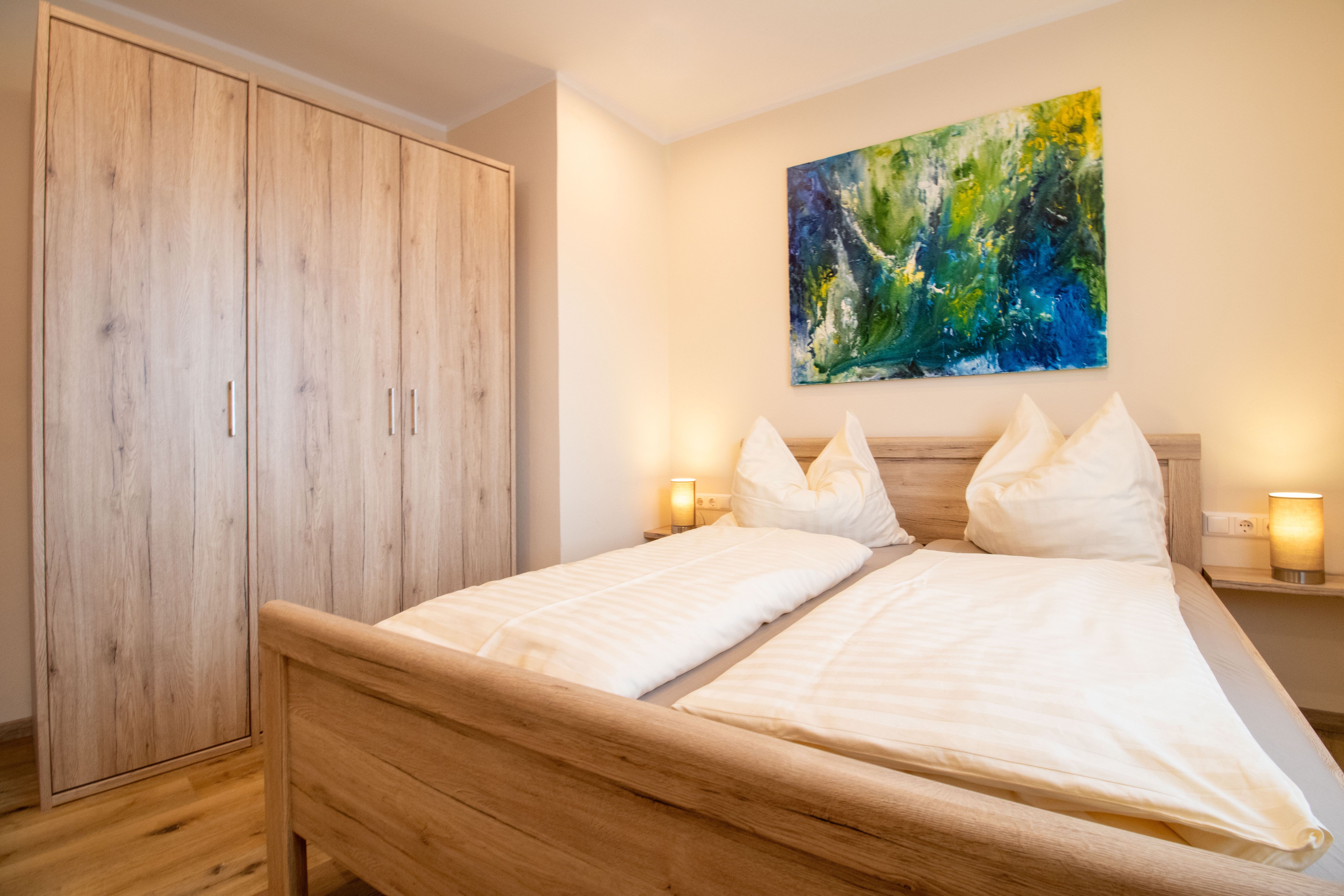 Ein gemütliches Schlafzimmer mit einem Doppelbett, Holzmöbeln und einem bunten Gemälde an der Wand.