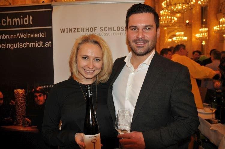 A couple holds a wine bottle and a wine glass in front of a banner with the inscription 'Winzerhof Schlosser'.