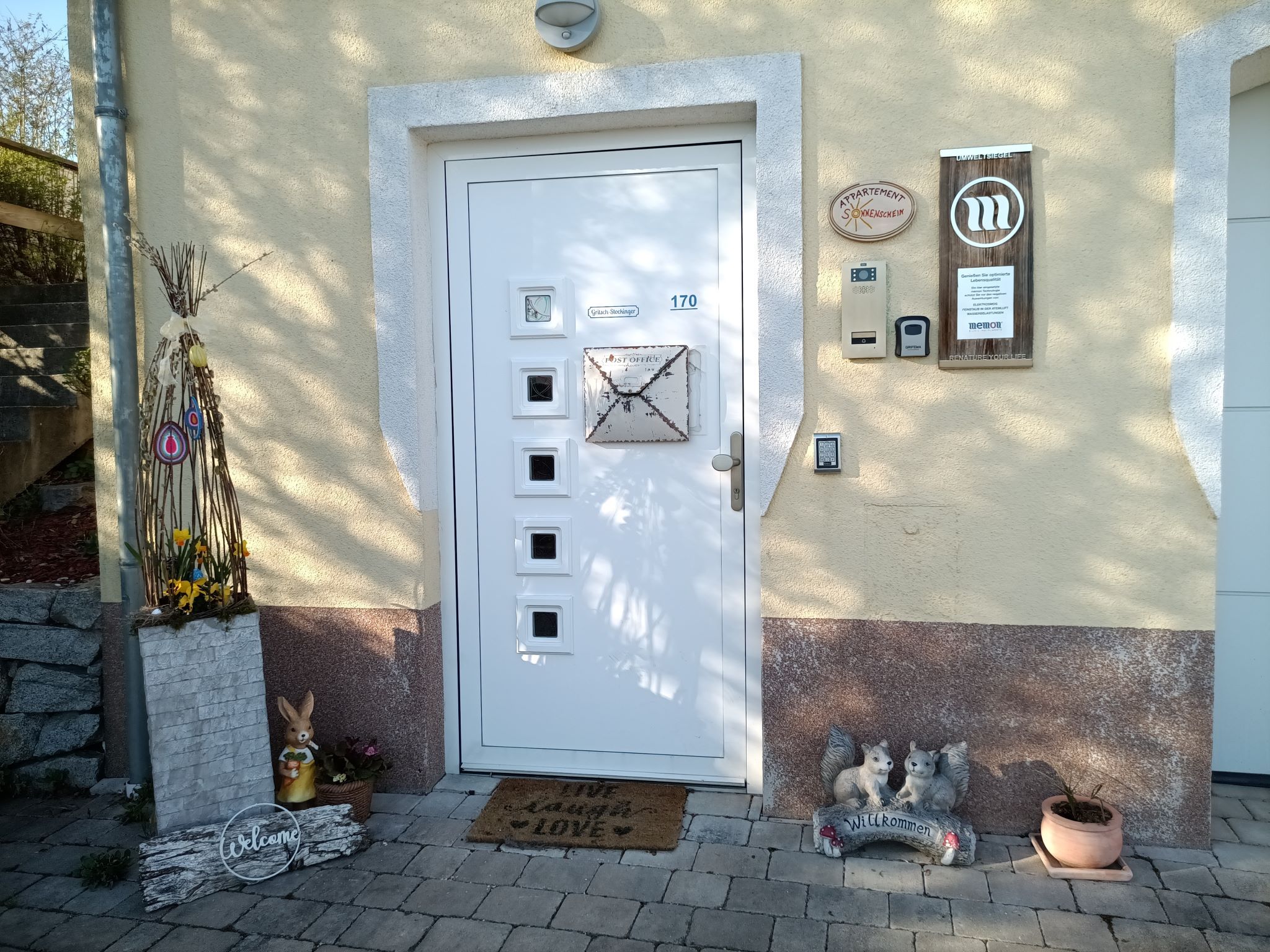 Eingangsbereich eines Hauses mit dekorativen Elementen wie einem Hasen, einem Willkommensschild und Blumen.