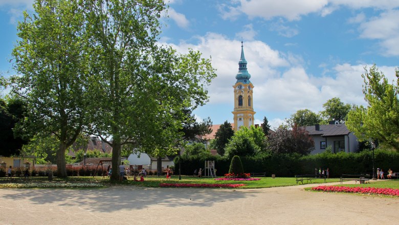 A park with flowerbeds, trees and a church tower in the background.