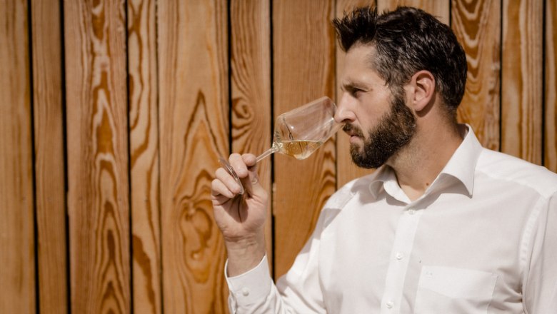 Mann riecht an einem Weinglas vor Holzwand.