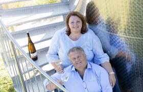 Ein Mann und eine Frau sitzen auf einer Metalltreppe mit Weingläsern in der Hand.