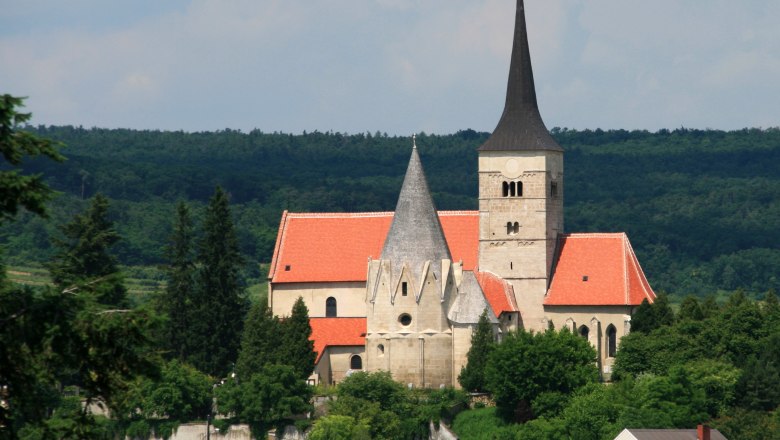St. Michaelskirche in Pulkau mit rotem Dach und spitzem Turm, umgeben von Bäumen.