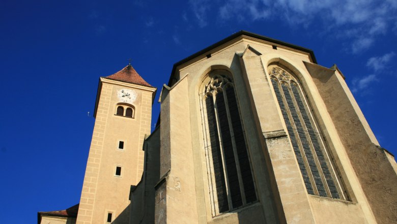 View of the Church of the Holy Blood in Pulkau with tower and Gothic windows against a blue sky.