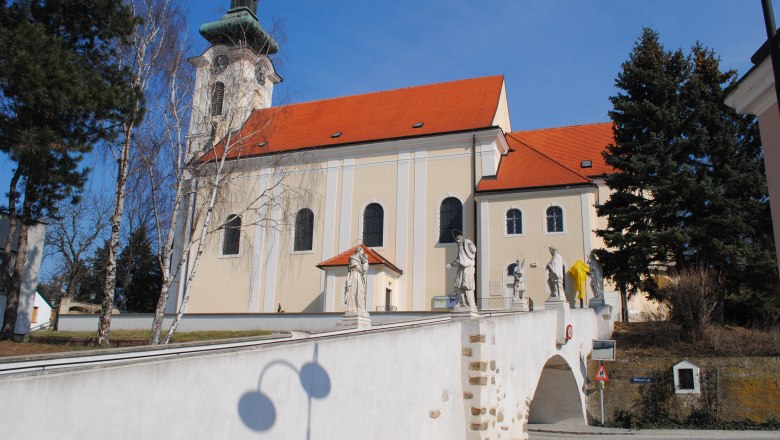 Pfarrkirche Wolkersdorf mit Statuen auf einer Br&uuml;cke, blauer Himmel.