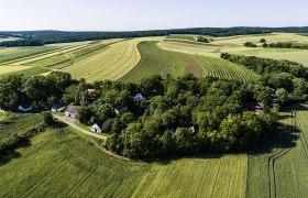 Luftaufnahme einer ländlichen Landschaft mit Feldern und einem kleinen Dorf umgeben von Bäumen.